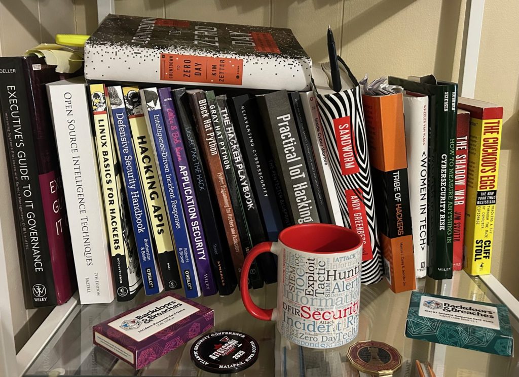 A bookshelf holds many books about cybersecurity, a coffee mug with security terms, playing cards